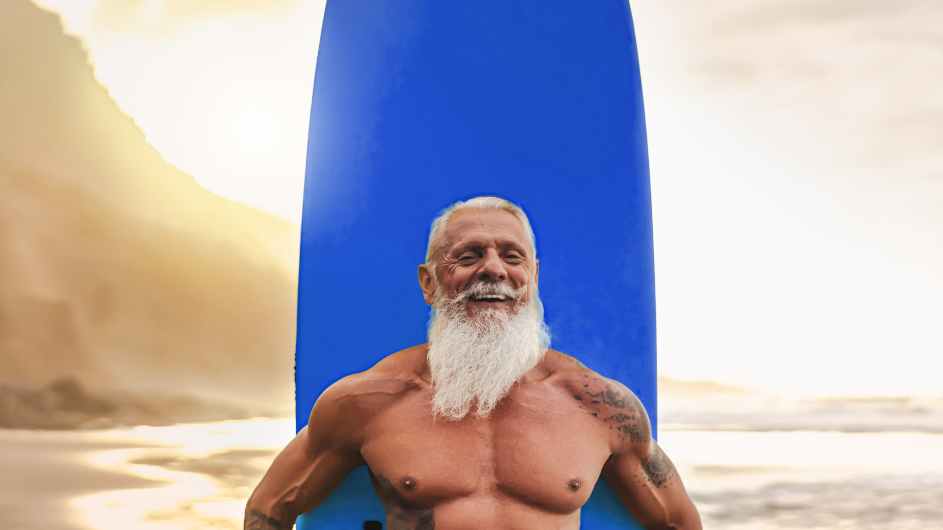 Muscular senior surfer smiling against blue surfboard